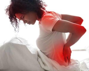 Woman with fibromyalgia pain sitting up in bed holding lower back. Fibromyalgia treating at Shoreside Interventional Pain in Sarasota, FL.